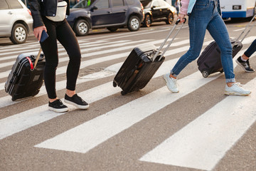 Cropped image of three women walking across pedestrian crossing, and carrying luggage after arrival...