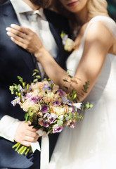Obraz na płótnie Canvas Hands of groom and bride at wedding day. Bridal couple hugging. Wedding bouquet at background. Wedding love and family concept close up macro photo with selective focus