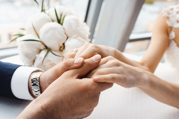 Hands of groom and bride at wedding day. Bridal couple hugging. Wedding bouquet at background. Wedding love and family concept close up macro photo with selective focus