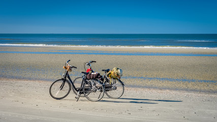 On a summer September afternoon on the beach of the Dutch Wadden Isle of Schiermonnikoog located in the Wadden Sea, two bikes are waiting for their owners.