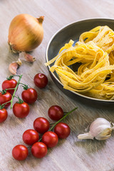 Ingredients for cooking pasta with tomatoes on a light wooden background - Fettuccine, cherry tomatoes, onions and garlic