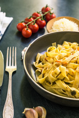 Traditional Italian fettuccine pasta with tomatoes in a rustic plate on a dark background