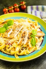 Traditional Italian organic pasta fettuccine with grilled chicken breast, tomatoes, parmesan cheese and basil in a rustic plate
