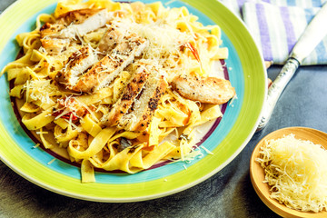 Traditional Italian chicken parmesan pasta - fettuccine with grilled chicken breast, tomatoes, parmesan cheese in the rustic plate
