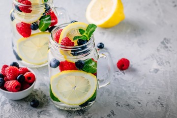 Infused detox water with lemon slice, raspberry, blueberry and mint. Ice cold summer cocktail or lemonade in mason jar
