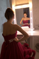 Attractive woman in a beautiful red dress looks in the mirror.