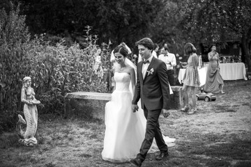 Just merried couple of groom and bride walking holding hands in the garden near the bushes. Wedding celebration