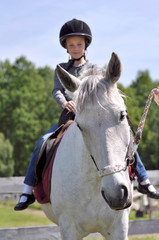 Young girl riding a white horse in a helmet