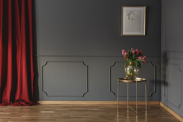Pink tulips on a golden table in the corner of a luxurious interior with molding on dark gray walls...