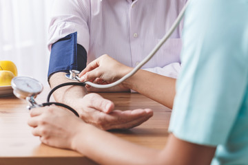 Closeup of patient's hand and a doctor measuring his blood pressure on a wooden desk