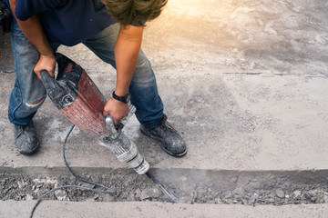 Male worker repairing driveway surface with jackhammer, digging and drilling concrete roads