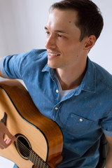 Handsome and cheerful guy musician in a shirt playing guitar