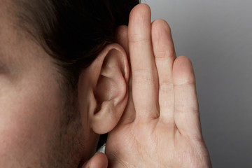 Listening male holds his hand near his ear over grey background.Closeup