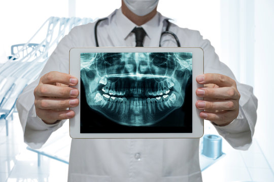 Dentist holding a digital tablet with x-ray of teeth in dental office