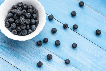 Fresh ripe blueberries in ceramic bowl on wooden table plank, top view