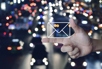 Mail icon on finger over blurred colourful night light city with cars, Contact us concept