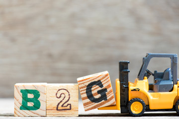Toy forklift hold letter block G in word B2G (abbreviation of business to government) on wood background