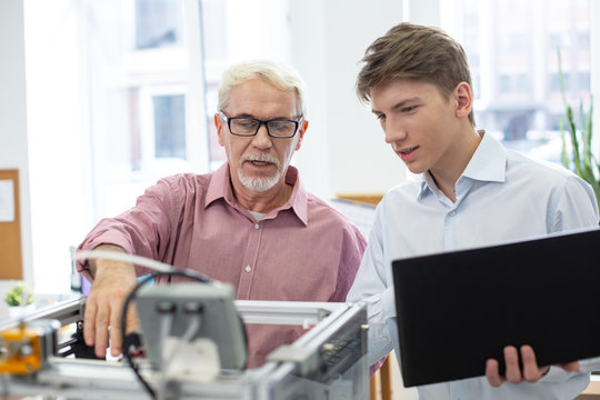 Nice teacher. White-haired senior engineer teaching his young student about 3D printers and telling him about the work algorithm