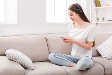 Young woman with cell phone and headphones on beige couch