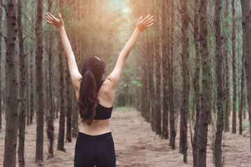 Fototapeta premium Women stretching arms and breathing fresh air in middle of pinewood forest while exercising. Workouts and Lifestyles concept. Happy life and Healthcare theme. Nature and Outdoors theme. Back view
