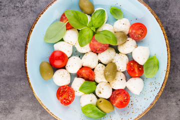 Delicious caprese salad with ripe cherry tomatoes and mini mozzarella cheese balls with fresh basil leaves.