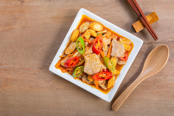 top view of stir fried pork with roasted chili paste in ceramic plate on wooden table. asian homemade style hot and spicy food menu.