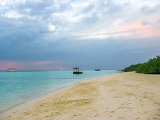 Maldives background. Sunset over the tropical sea and coral beach with colorful cloudy sky. Boats on the horizon. North Male Atoll Asdu, Indian Ocean.
