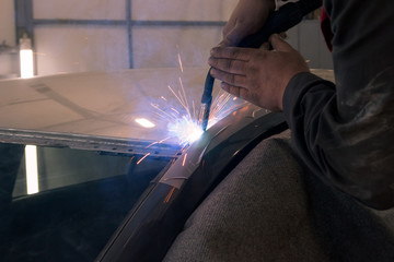 Experienced man performs work on body repair car with a welding machine. Repair of the roof of the vehicle.