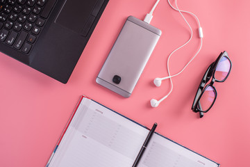 Laptop, glasses, pen, notebook and phone with headphones on pink pastel background. Top view. Concept of planning