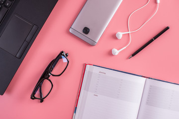 Laptop, glasses, pen, notebook and phone with headphones on pink pastel background. Concept of planning