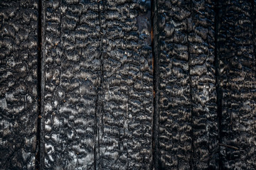 Texture of charred burnt wood board wall after fire, black coal background