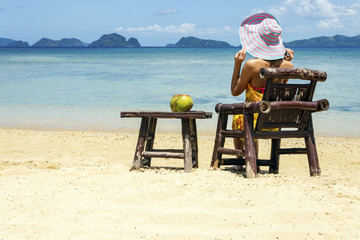 A girl sitting on a bamboo chair on the beach on a blue sea and sky background. place for text.