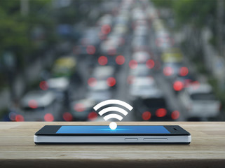 wi-fi button flat icon on modern smart phone screen on wooden table over blur of rush hour with cars and road, Technology and internet concept