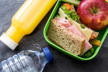 Healthy school lunch box: Sandwich, vegetables ,fruit and juice on black stone. Top view