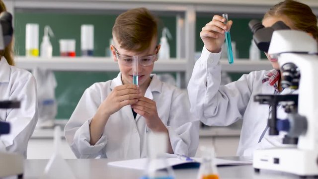 education, science and children concept - teacher and students with test tubes studying chemistry at school laboratory