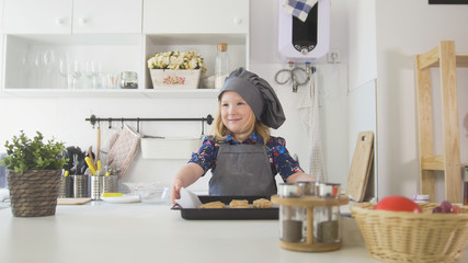 Fototapeta na wymiar Preschool girl baker holding a baking sheet with cookies