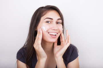 Close-up face of beautiful woman applying moisturiser cream on her cheek