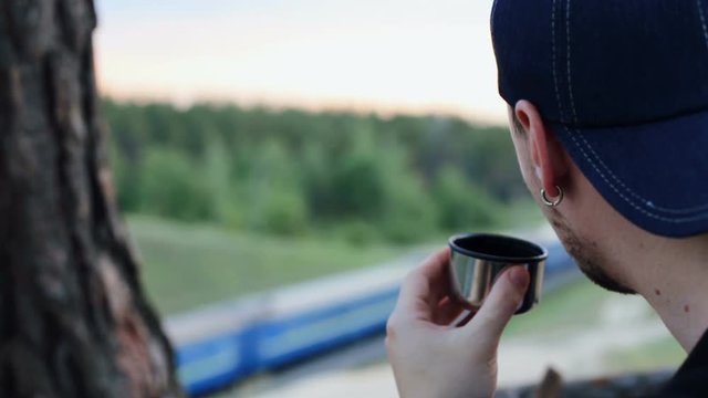 A young man drinks tea from a thermos in the forest area