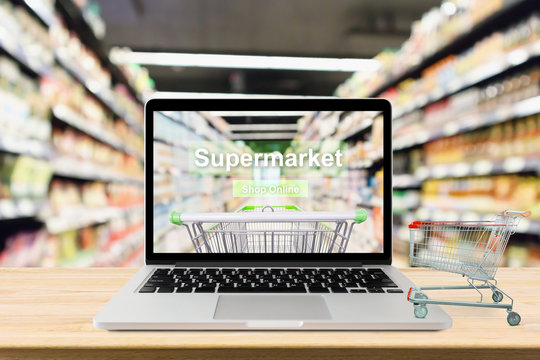 laptop computer on wood table with supermarket aisle blurred background online shopping concept