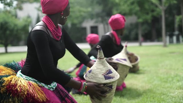 African women are dancing a folk traditional dance on a grass meadow, in traditional costumes with wicker baskets, sunny, trees' background, African costumes, traditions, African culture, tribes