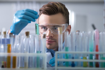 Young interested scientist keeping and overlooking test tube.