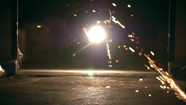 Male silhouette performs flips among the sparks from grinder at night