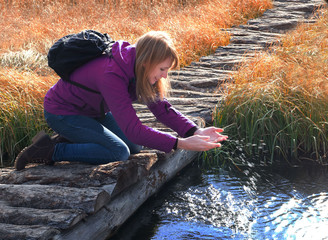 A young woman is playing with water in a creek. Sun rays on the spray of water.