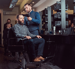 Professional barber working with a client in a hairdressing salon, uses a hair dryer.