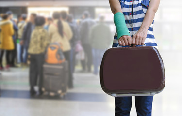 green cast on hand and arm with suitcase isolated on blurred traveler and bag waiting in subway, insurance travel concept