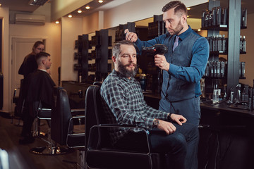 Professional barber working with a client in a hairdressing salon, uses a hair dryer.