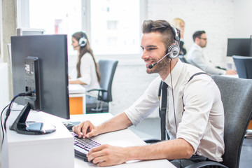 Handsome man in business wear with headset using computer in call center - obrazy, fototapety, plakaty
