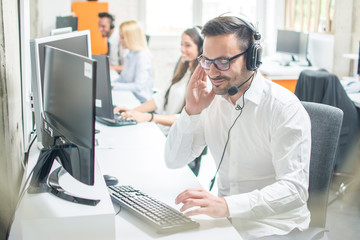 Young man in shirt with headset using computer in a bright office