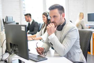 Confused or worried business man with eyeglasses in hand looking at computer screen in office