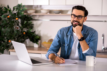 Joyful man making notes in the kitchen